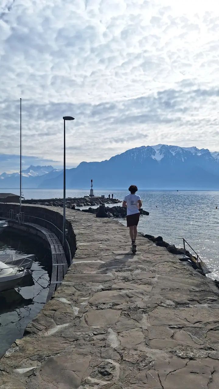 Naji court sur une jetée au bord du Léman, t-shirt CST+, montagnes en arrière-plan